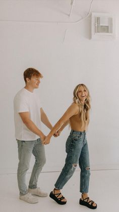 a man and woman holding hands while standing next to each other in front of a white wall