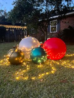 christmas ornaments on the grass in front of a house with string lights and fairy lights