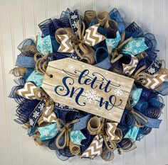 a wreath that says let it snow on the front door with blue and brown ribbons