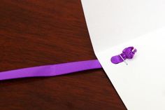 a piece of paper with a purple ribbon attached to it on top of a wooden table