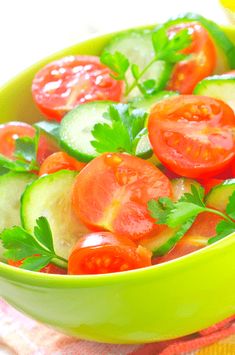 a green bowl filled with cucumbers and tomatoes