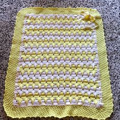 a yellow crocheted dishcloth sitting on top of a gray floor next to a black and white cat