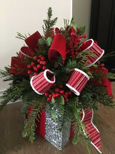 a christmas arrangement in a silver vase with red ribbon and evergreens on the side