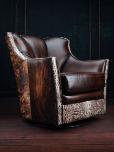 a brown leather chair sitting on top of a wooden floor next to a black wall