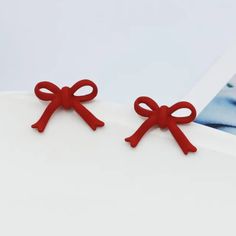 pair of red bow - shaped earrings on white paper with photo in the back ground