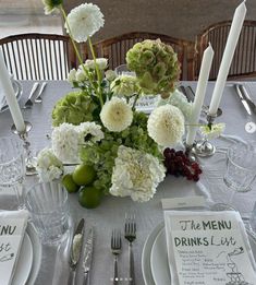 the table is set with white and green flowers, silverware, and menus