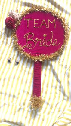 a pink sign that says team bride on it with some flowers in the middle and gold strips around it