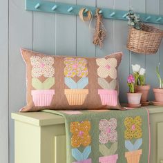 a decorative pillow on a bench next to potted plants and a basket with flowers