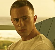 a man sitting in a chair looking at the camera with an ocean view behind him