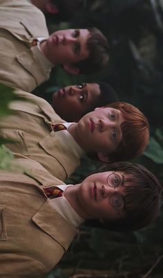 the three young men are standing in front of some plants and trees, one is wearing a brown suit