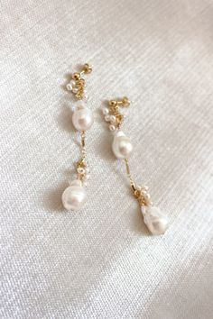 two pairs of earrings with pearls hanging from the side on a white fabric background,