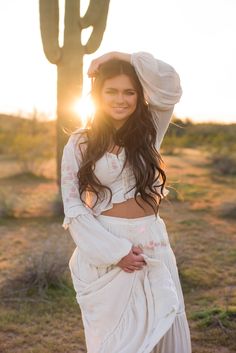 a woman standing in front of a cactus with the sun shining through her hair and wearing a white dress