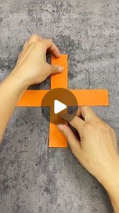 someone is cutting out an orange piece of paper to make the shape of a cross