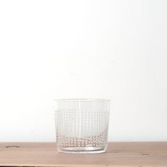 a clear glass sitting on top of a wooden table next to a white wall in the background