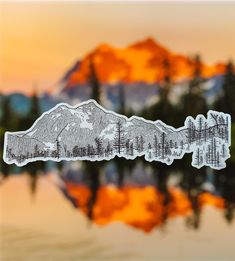 a sticker with trees and mountains on it in front of a body of water