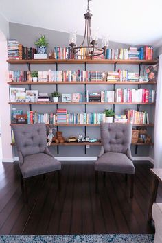 two gray chairs sitting in front of a book shelf