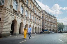 a man and woman walking down the street in front of an old building with arches