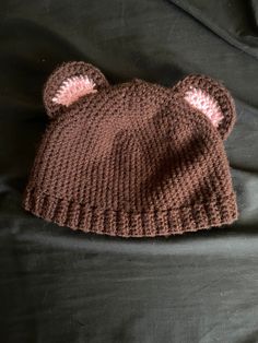 a brown knitted bear hat laying on top of a black bed sheet with two ears