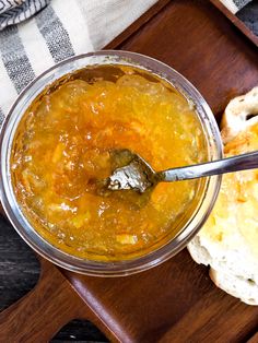 a spoon in a glass bowl on top of a wooden tray filled with food and bread