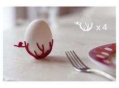 an egg with red antlers is sitting on the table next to a fork and knife