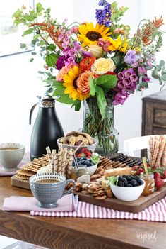 a wooden table topped with lots of different foods and flowers in vases on top of it