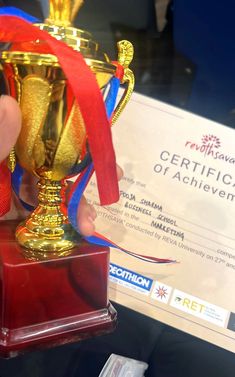 a person holding up a golden trophy with a red ribbon around it's neck