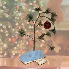 a small christmas tree with a red ornament on it's branch and a book