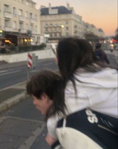 two people walking down the street with buildings in the background and one person wearing a backpack