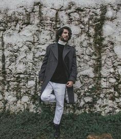 a man standing in front of a stone wall with ivy growing on it's sides