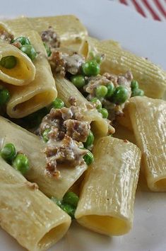 a white plate topped with pasta covered in meat and peas next to a red striped table cloth