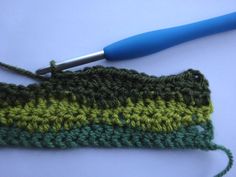 a crocheted green and yellow piece of cloth with a blue handled knitting needle