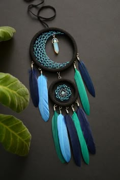 three pieces of jewelry with feathers hanging from them on a table next to a plant