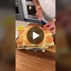 a person cutting up a sandwich on top of a wooden board with a knife in it