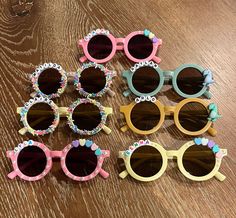 six pairs of children's sunglasses with bows on them sitting on a wooden table