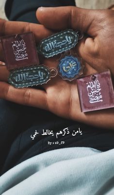 the person is holding five different key chains in their hands with arabic writing on them