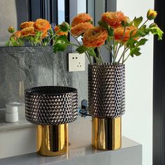 two gold vases with flowers in them on a counter top next to a mirror