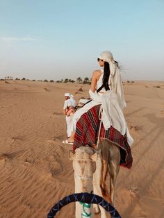 a woman riding on the back of a camel in the middle of the desert,