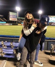 a man is hugging a woman in the stands at a baseball game with stadium lights behind him