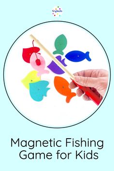 a hand holding a wooden stick with colorful fish on it and the words magnetic fishing game for kids