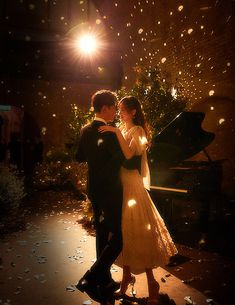 a bride and groom standing in front of a grand piano at night with lights on