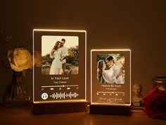 an illuminated photo frame with two photos on it and a vase full of flowers in the background