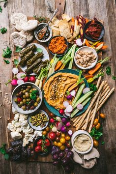 an assortment of food is laid out on a wooden table, including vegetables and dips