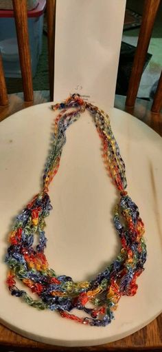 a multicolored necklace sitting on top of a white plate next to a wooden chair