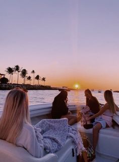 three women sitting on the back of a boat in the ocean at sunset with palm trees