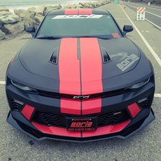 a red and black chevrolet camaro parked in a parking lot next to the ocean