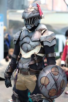 a man dressed in armor and holding a skateboard on the street with other people walking behind him