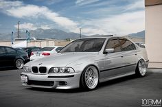 a silver car parked in a parking lot next to other cars and buildings with mountains in the background