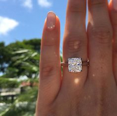 a woman's hand with a diamond ring on top of her finger and palm trees in the background