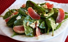 a white plate topped with spinach and grapefruit salad next to a red table cloth