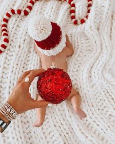 a person holding a red ornament on top of a white knitted blanket